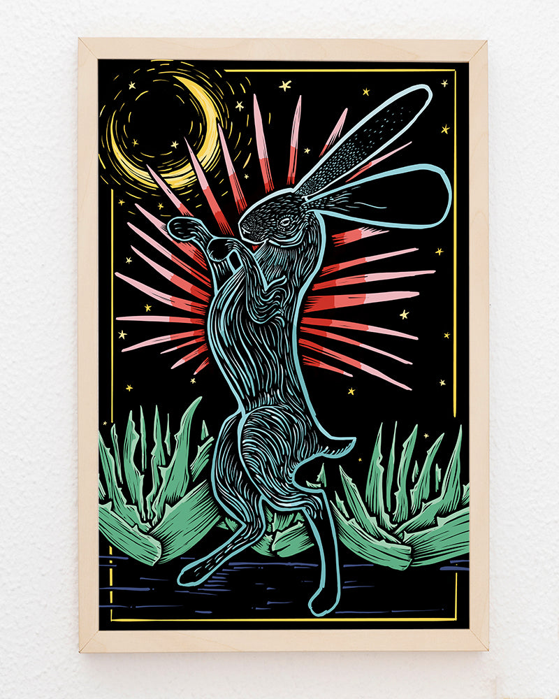 Framed artwork of a stylized rabbit with large ears in front of agave plants against a night sky with stars and moon.