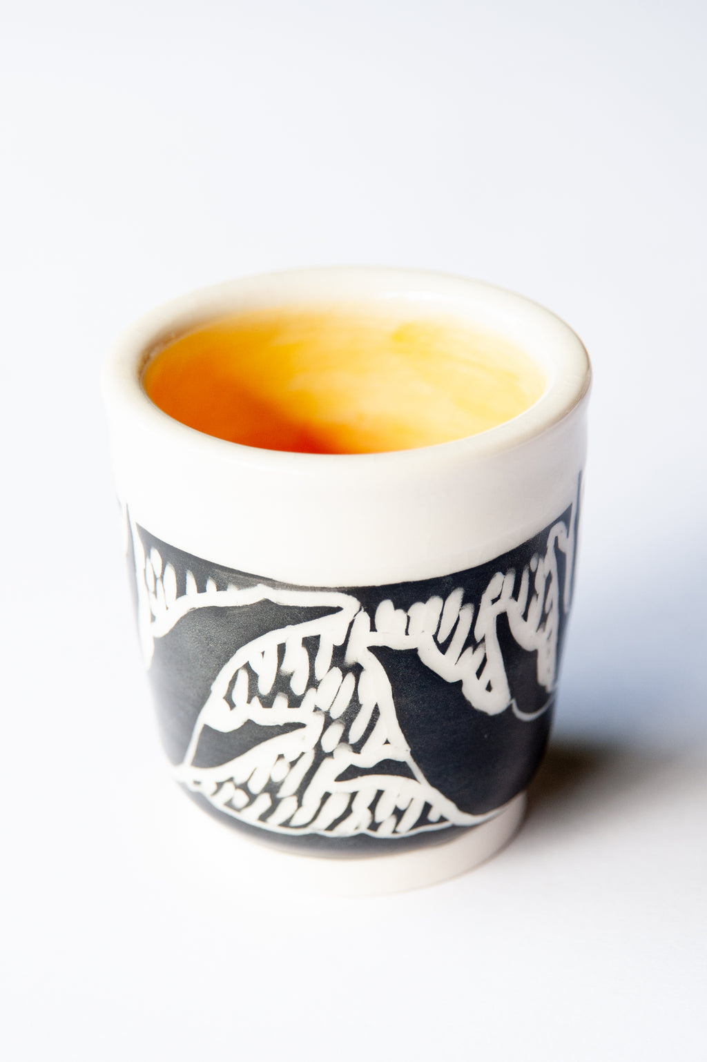 A small ceramic cup with a black and white agave block print design, set against a plain white background.