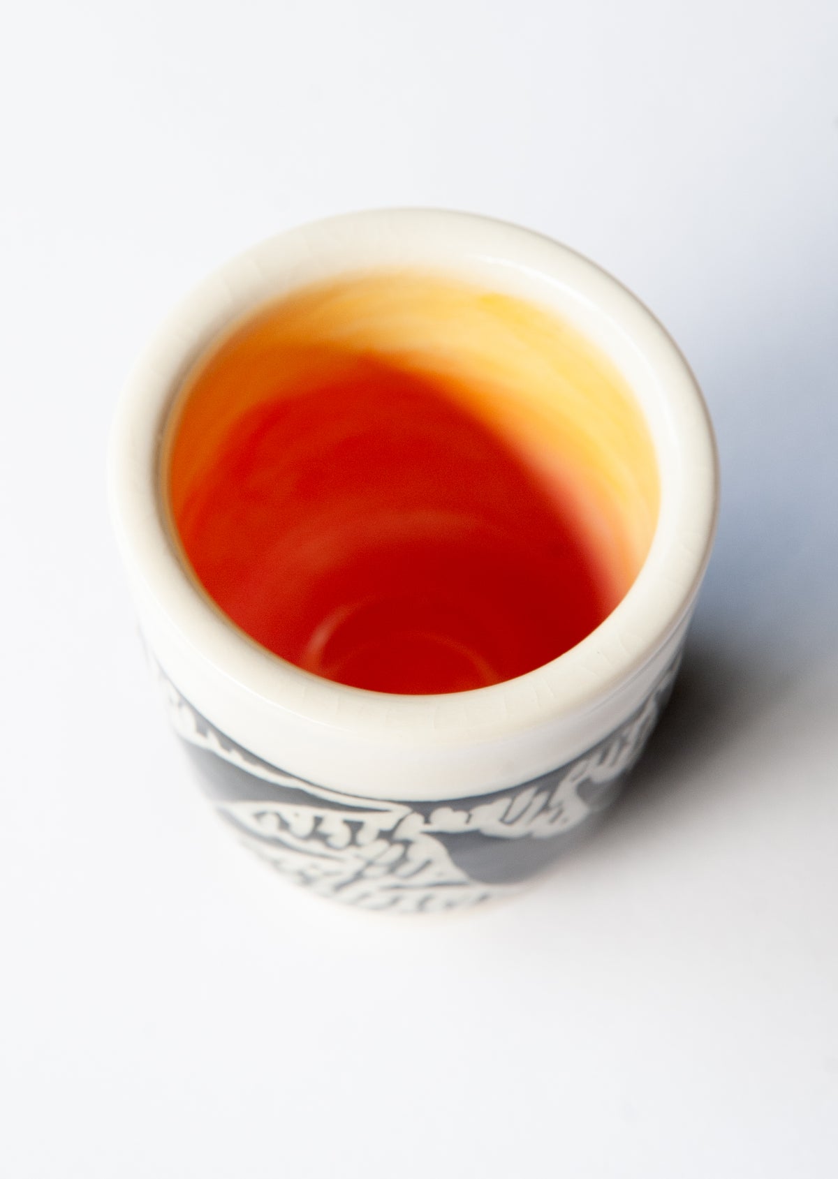 A small ceramic cup viewed from above, with a bright orange-red interior, on a plain white background.