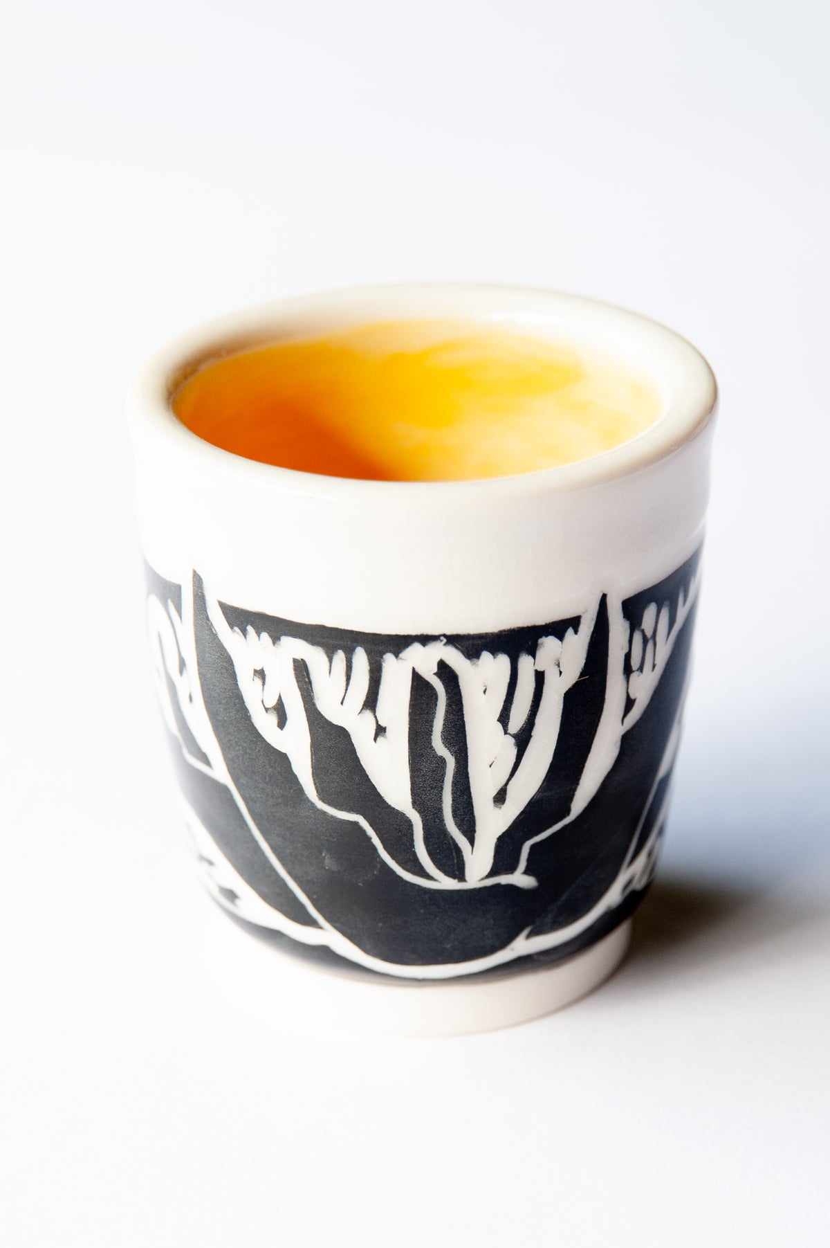 A small ceramic cup with a black and white agave block print design, set against a plain white background.