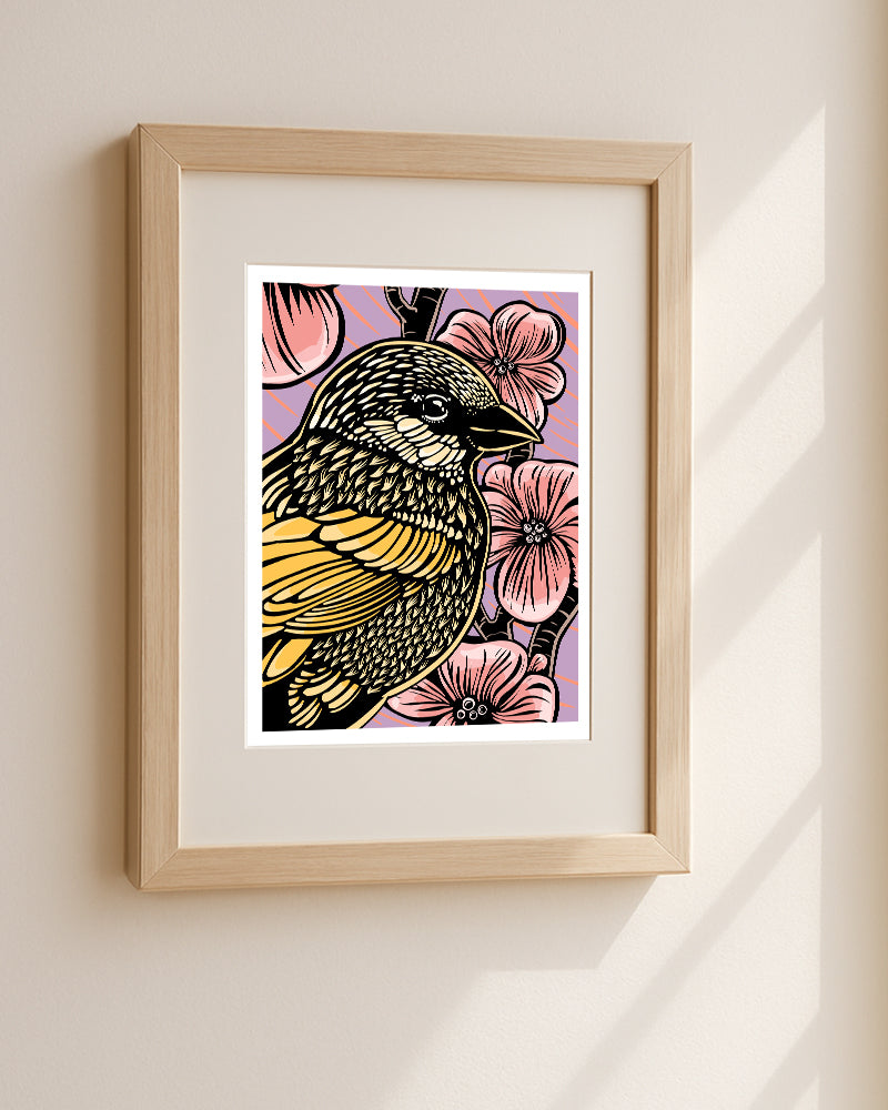 Framed wall art featuring a stylized  illustration of a sparrow with yellow and black patterned feathers, surrounded by pink flowers on a purple background displayed in a light wood frame against a beige wall with soft window shadows.