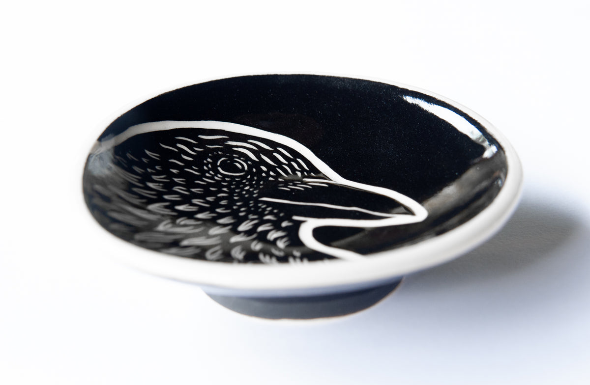 A small black ceramic bowl featuring a white crow design on the inside, set against a plain white background.
