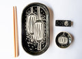 A set of black and white ceramic tableware featuring a hand-drawn lantern pattern, arranged on a white background alongside a pair of wooden chopsticks. The set includes a large oval platter, a small bowl, and a chopstick rest.