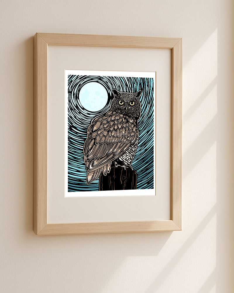 Framed owl art print with a stylized owl illustration under a full moon, mounted on a light wood frame with a white mat against a beige wall.