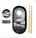 Ceramic set with Mount Fuji design, including a large plate, smaller bowl, chopstick holder,  and chopsticks on a white background.