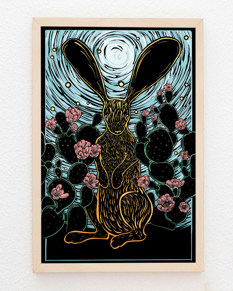 Framed artwork of a stylized rabbit with large ears standing in front of prickly pear cactus on a blue and black background.