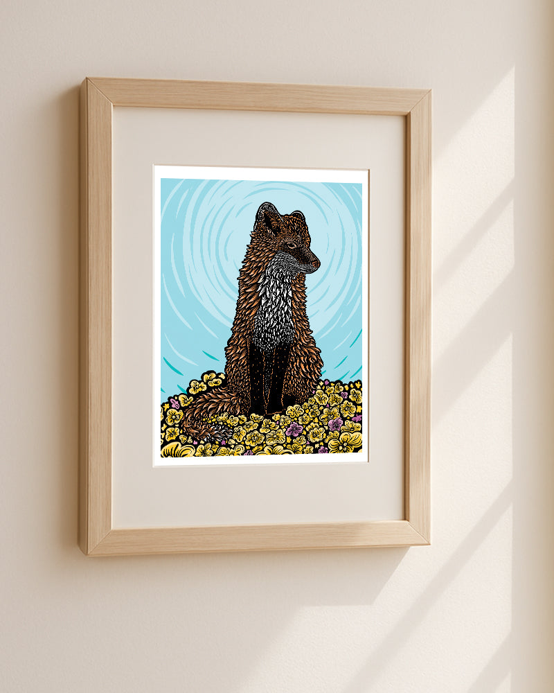 Woodblock style print of a red fox sitting in a field of yellow and magenta flowers against a blue background, displayed in a light wood frame on a beige wall.