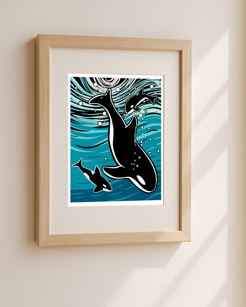 Framed wall art featuring a stylized print of three orcas and bubbles on a blue water background, displayed in a light wood frame on a beige wall.